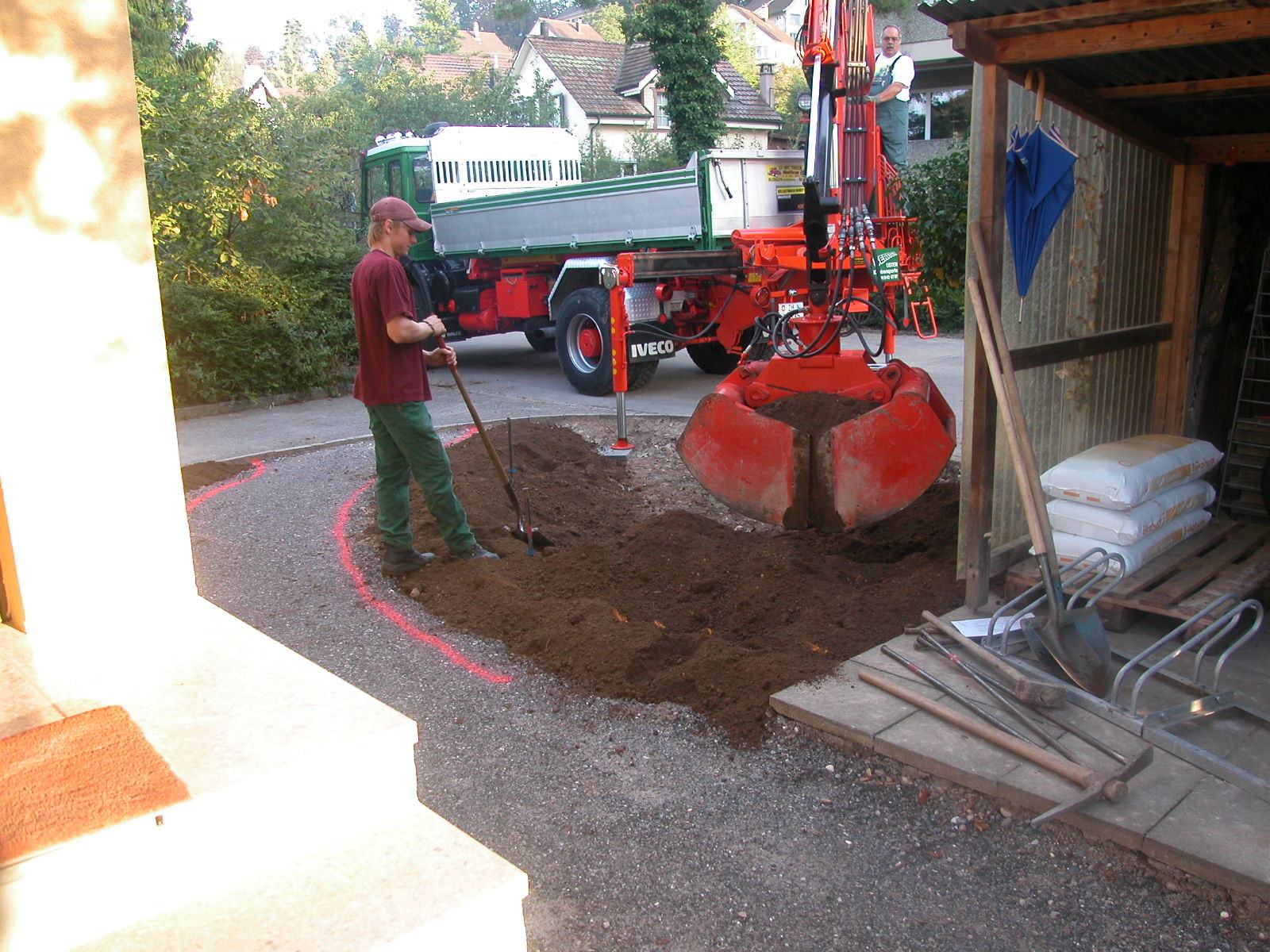 Team beim Erdarbeiten neben einem Kipper vor einem Gartenhaus